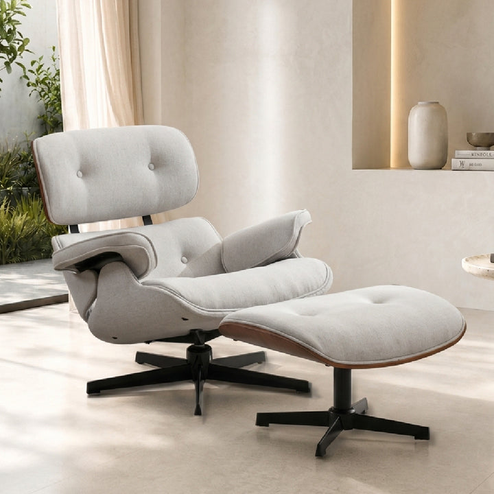 A modern lounge chair with matching ottoman in light beige fabric, shown in a bright, minimalist interior setting with warm natural light.