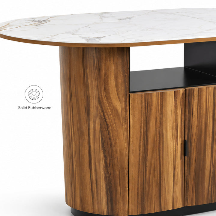 Close-up of a modern island table with a white sintered stone top, warm brown wood grain cabinet base, opened shelf and base trim, and a small 'Solid Rubberwood' badge on the left.