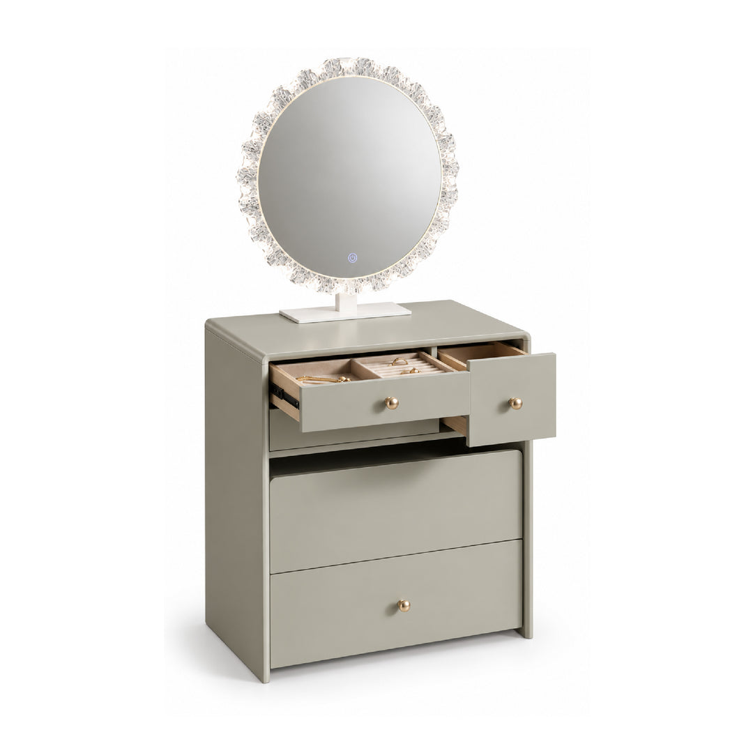 A light gray vanity table with three drawers, one of which is open to reveal jewelry compartments, topped with a round mirror featuring a crystal-like floral frame.