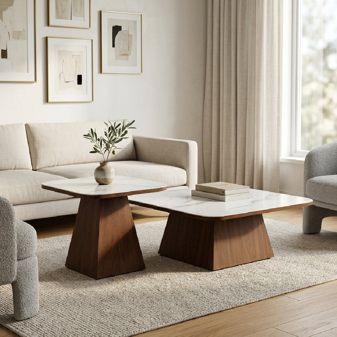 A modern living room scene featuring a two-tier coffee table with a white marble-patterned top and a wide, angled dark walnut wood base, styled on a textured rug next to a cream sofa.