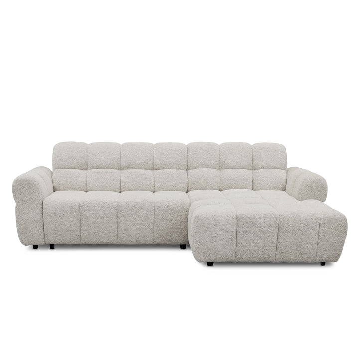 A modern l-shape sofa upholstered in a textured light grey bouclé fabric, featuring a tufted backrest and a right-side chaise lounge, shown against a plain white background.