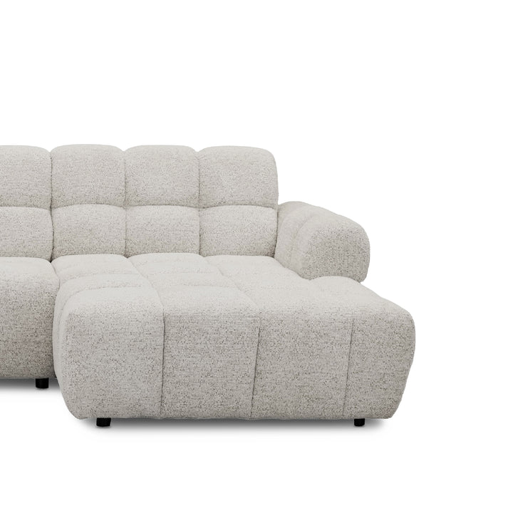 A closeup photo of modern l-shape sofa with a chaise lounge, upholstered in a textured boucle fabric in a light grey shown against a plain white background.