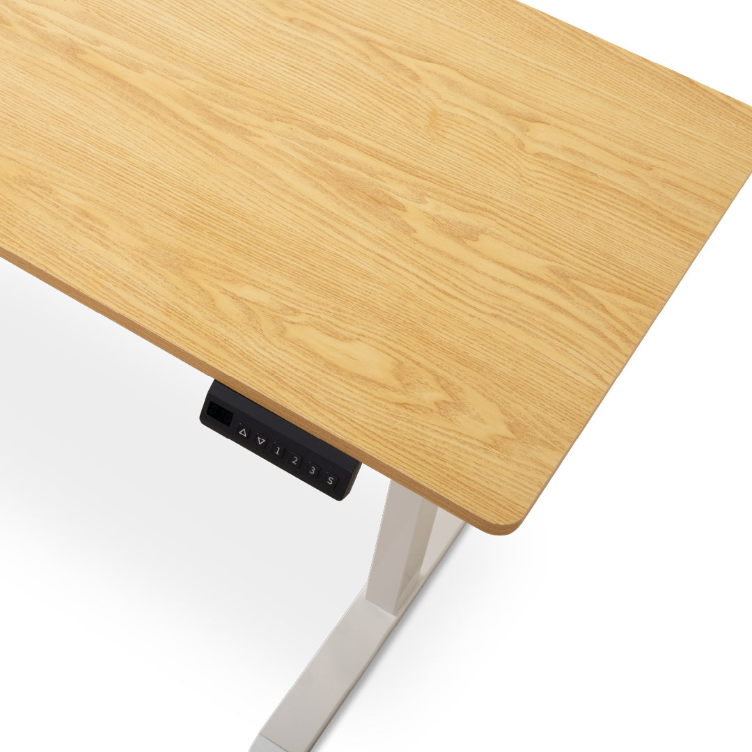 Close-up of a light oak wood desktop with a white metal leg and a black electronic control panel showing speed settings, on a white background.