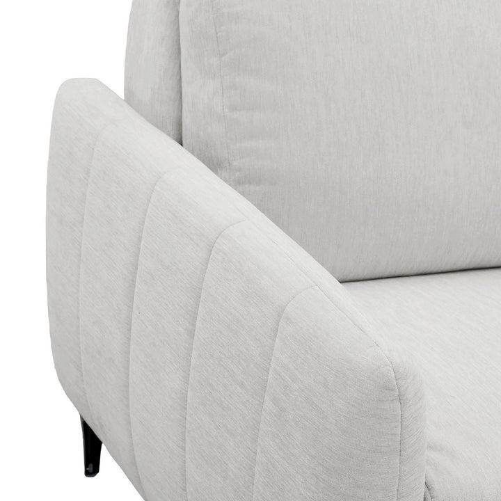 Close-up of a light khaki upholstered armchair showing the armrest with vertical channel tufting, the back cushion, and part of the seat, on a white background.
