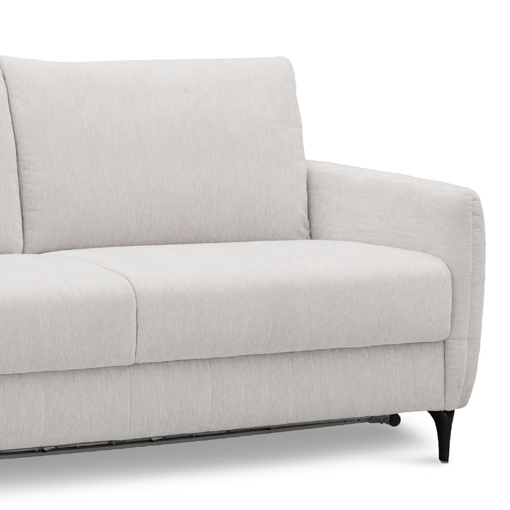 A close-up of a light khaki upholstered sofa-bed showing the back cushion, seat, armrest, and a small black leg on a white background.