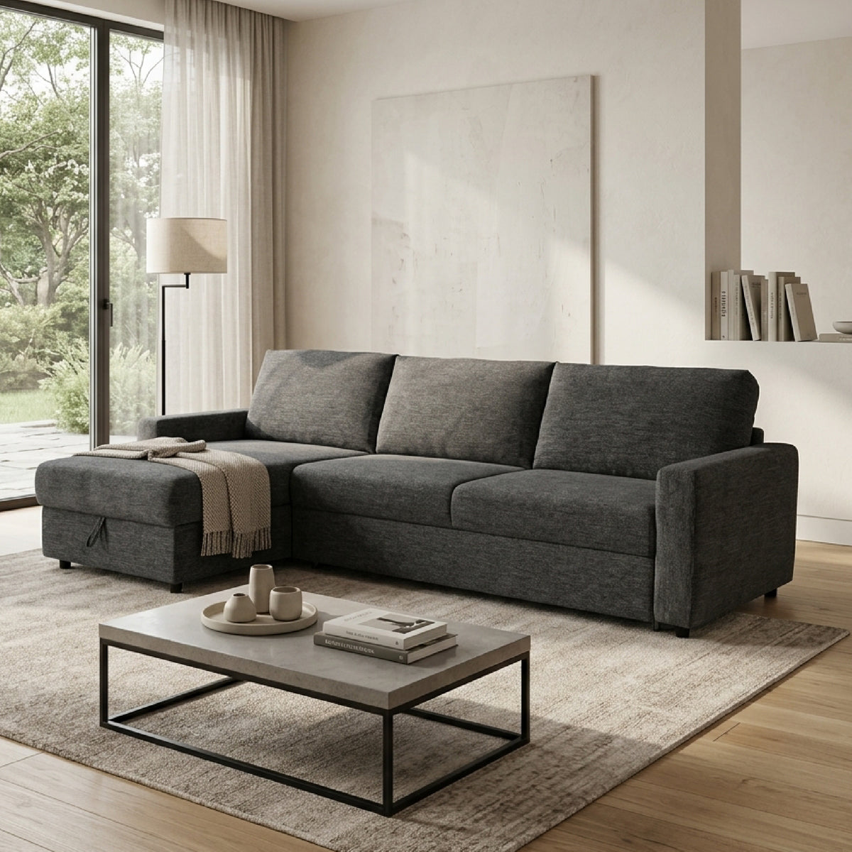A modern L-shaped sectional sofa-bed in dark gray textured fabric, styled in a bright, contemporary living room with a low coffee table, neutral rug, and large window view.