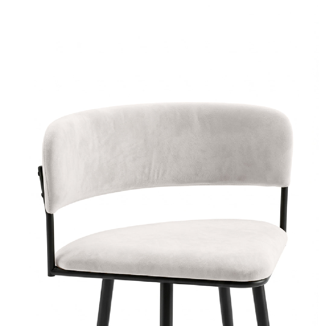 A modern bar stool featuring a curved backrest and seat cushion upholstered in light beige velvet, supported by a slim black metal frame.