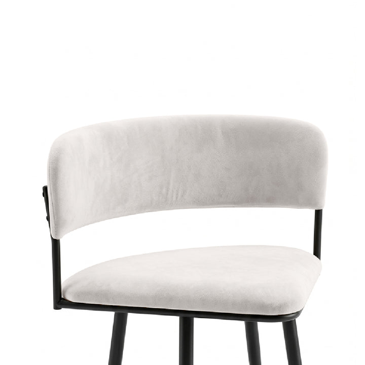 A modern bar stool featuring a curved backrest and seat cushion upholstered in light beige velvet, supported by a slim black metal frame.