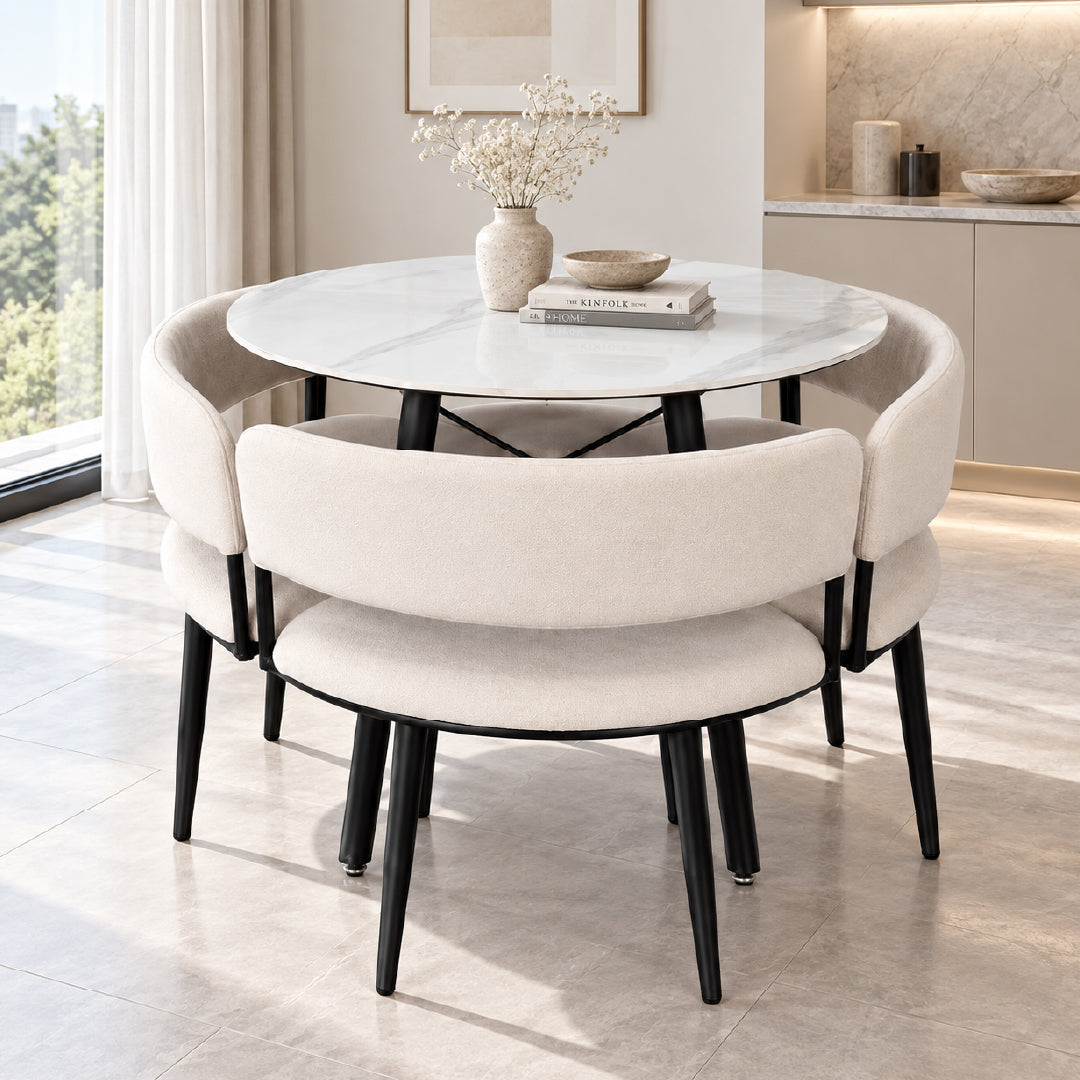 A modern round dining table with a white marble-look top and black legs, surrounded by four upholstered dining chairs in a warm off-white fabric with black legs, set in a bright, contemporary dining room.